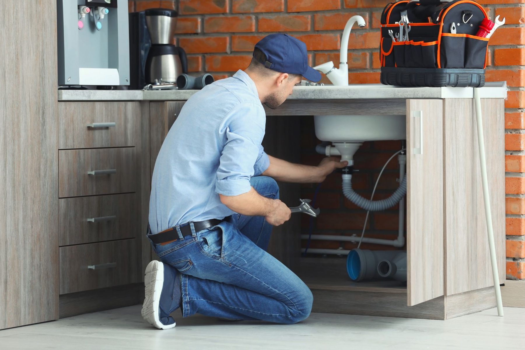 Plumber kneeling to repair the drain under a kitchen sink